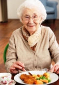 Seniorin lachend vor einem Teller mit Essen
