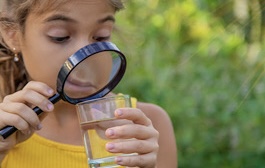 Mädchen schaut mit einer Lupe in ein Glas Wasser