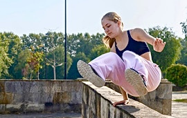 Mädchen in rosa Jogginghose macht Parkours auf einer Mauer
