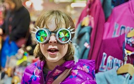 Mädchen auf einem Flohmarkt mit sehr ausgefallener Brille mit Stacheln schaut in die Kamera