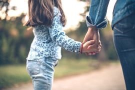 Rückansicht Mutter und hüpfende Tochter an an der Hand, die einen Weg laufen