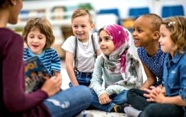 Kinder unterschiedlicher Herkunft auf dem Boden sitzend bekommen vorgelsesen