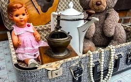 eine alte Puppe, eine Kanne und ein alter Teddy in einem alten Koffer