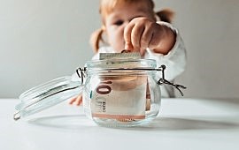 Kleines Mädchen mit Zöpfen macht eine Münze in eine Glas mit Geld