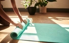 Frauenhände rollen eine Yogamatte aus im Hintergund Sonnenlich und zweiZimmerpflanzen