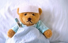 Teddy mit Verband und Fieberthermometer im Bett