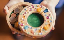 Kinderhände halten eine runde Geldschatulle mit Glitzerperlen