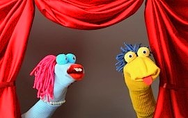 Zwei bunte Sockenpuppen auf einer Bühne mit rotem Theatervorhang